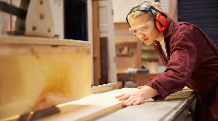 Female Apprentice Using Circular Saw In Carpentry Workshop